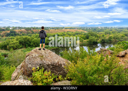 Ein Jugendlicher steht auf einem großen Stein Boulder am Ufer des südlichen Bug Fluss und sieht am Horizont. Der südliche Bug Fluss in der Summe Stockfoto