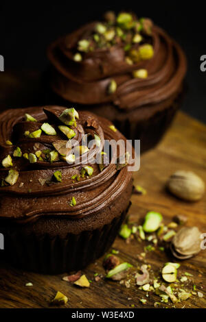 Schöne Schokolade cupcakes gekrönt mit Chocolate buttercream dekoriert Pistazie auf dunklem Hintergrund. Hausgemachte Desserts. Dunkle Essen Stockfoto