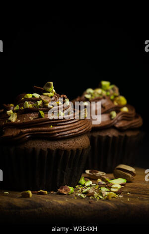 Schöne Schokolade cupcakes gekrönt mit Chocolate buttercream dekoriert Pistazie auf dunklem Hintergrund close-up mit Platz für Text kopieren Stockfoto