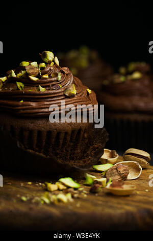 Schöne Schokolade cupcakes gekrönt mit Chocolate buttercream dekoriert Pistazie auf dunklem Hintergrund. Hausgemachte Desserts. Dunkle Essen Stockfoto