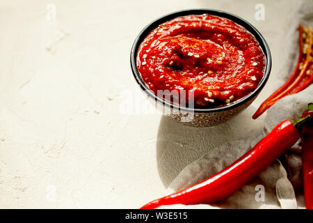 Traditionelle hausgemachte rose Harissa - Hot Chili Pepper Sauce Paste mit Knoblauch und Olivenöl in kleinen Schüssel auf weißem Putz Hintergrund mit Kopie Raum Stockfoto