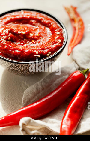 Traditionelle hausgemachte rose Harissa-maghrebinischen red hot chili Paste mit Knoblauch und Olivenöl in kleinen Schüssel auf weißem Putz Hintergrund close-up Stockfoto