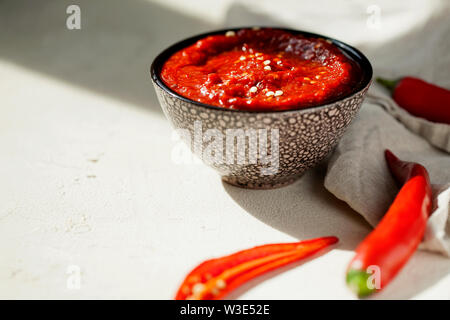 Traditionelle hausgemachte rose Harissa - Hot Chili Pepper Sauce Paste mit Knoblauch und Olivenöl in kleinen Schüssel auf weißem Putz Hintergrund mit Kopie Raum Stockfoto