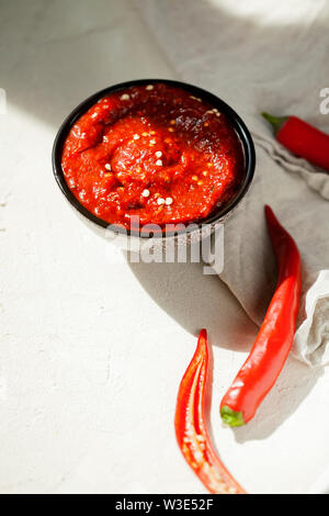 Traditionelle hausgemachte rose Harissa - Hot Chili Pepper Sauce Paste mit Knoblauch und Olivenöl in kleinen Schüssel auf weißem Putz Hintergrund mit Kopie Raum Stockfoto