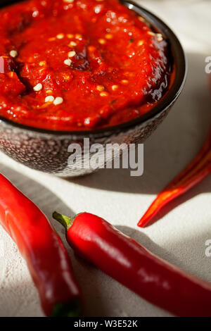 Traditionelle hausgemachte rose Harissa-maghrebinischen red hot chili Paste mit Knoblauch und Olivenöl in kleinen Schüssel auf weißem Putz Hintergrund close-up Stockfoto