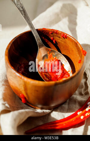 Traditionelle hausgemachte Harissa-maghrebinischen red hot chili Paste mit Knoblauch und Olivenöl in der Löffel und Schüssel close-up. Tunesien und arabische Küche adjika Stockfoto