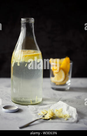 Selbstgemachte erfrischende infundiert detox Wasser oder Limonade in Glasflaschen mit geriebenem Ingwer und Zitronensaft auf dunklem Hintergrund close-up mit Platz für Text kopieren Stockfoto