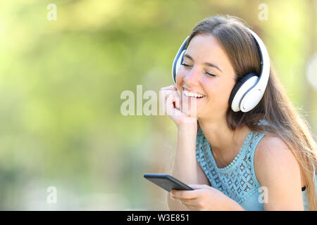 Happy girl entspannende Musik hören mit Smart Phone in einem Park mit grünem Hintergrund Stockfoto