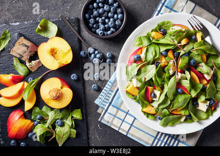Salat mit frischen Mangold Blätter, Pfirsich, Blaubeeren, Stücke von Gorgonzola Käse auf einem weißen Teller auf einen konkreten Tisch mit Zutaten serviert, Schmierfilm Stockfoto