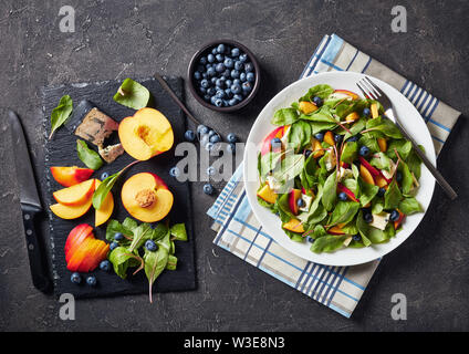 Salat mit frischen Mangold Blätter, Pfirsich, Blaubeeren, Stücke von Gorgonzola Käse auf einem weißen Teller auf einen konkreten Tisch serviert, horizontale Ansicht von oben Stockfoto