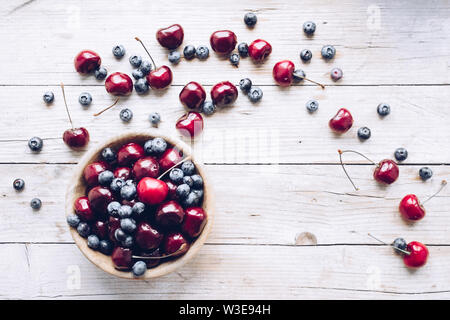 Schüssel von reifen Kirschen und Heidelbeeren. Große Sammlung von frisch gepflückte reife Beeren auf Holz- Hintergrund. Kopieren Sie Platz. Stockfoto