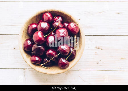 Schüssel von reifen Kirschen mit Stängeln. Große Sammlung von Frische rote reife Kirsche auf Holz- Hintergrund. Ansicht von oben. Kopieren Sie Platz. Stockfoto