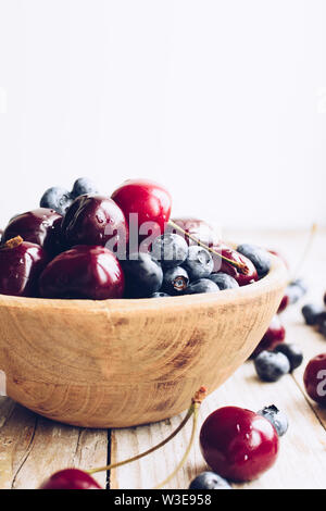 Schüssel von reifen Kirschen und Heidelbeeren. Große Sammlung von frisch gepflückte reife Beeren auf Holz- Hintergrund. Kopieren Sie Platz. Stockfoto