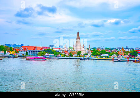 Die malerische Aussicht am Ufer des Chao Phraya Fluss mit herrlichen alten Wat Arun Tempel und der belebten Uferpromenade mit der Pier vor Es Stockfoto