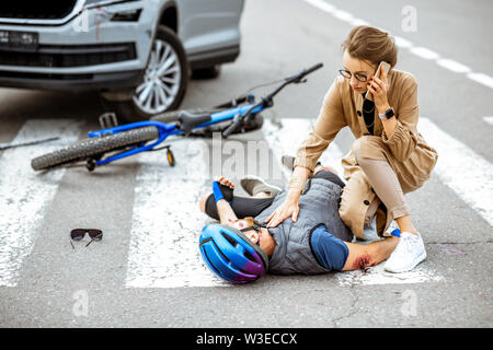 Verkehrsunfall mit Verletzten Radfahrer liegen auf dem Fußgängerüberweg in der Nähe der defekten Fahrrad, besorgt, Frau Treiber aufrufen und Überprüfen der Männer Puls Stockfoto