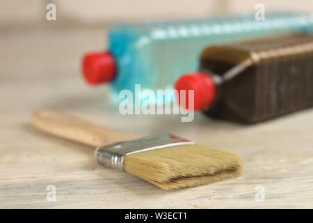 Eine Bürste liegt neben der Plastikflaschen mit Fleck und Lösungsmittel auf einem alten White vintage Holzbrett Tabelle. Für Text oder Logo. Stockfoto