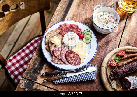 Buffet mit Wildbret Würstchen auf einem Holzbrett mit Mittagessen Teller mit geschnittenem Fleisch und Käse serviert mit Schwarzbrot und Salat Seiten und einem Becher Stockfoto