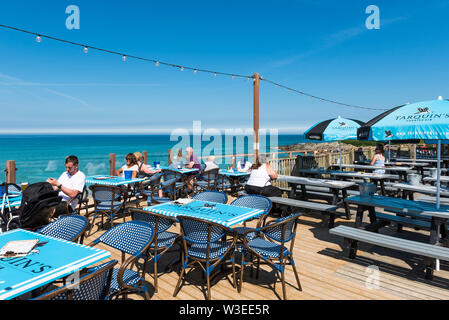 Urlauber sitzen auf der Terrasse des Fistral Beach Bar und entspannen in der Mitte Morgen Sonnenschein in Newquay in Cornwall. Stockfoto