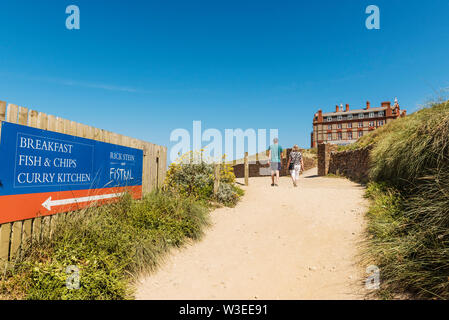 Urlauber zu Fuß entlang der Küste an der Rückseite des Headland Hotel an Fistral in Newquay in Cornwall. Stockfoto