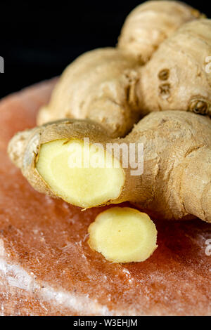 Frischer Ingwer Wurzeln auf persischen rosa Salz board schließen bis auf schwarz Holz- Hintergrund, Asian Food Konzept Stockfoto