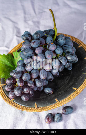 Bündel von Reifen blau-schwarz Tafeltrauben mit Blatt auf blauen Platte als süsse Frucht Dessert Stockfoto