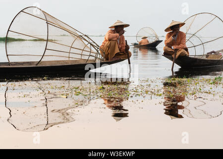 Inle, Myanmar - März 2019: Traditionelle Burmesische Bein rudernden Fischer bei der Inle See bei Sonnenaufgang. Das Sitzen auf dem Boot und Rauchen. Stockfoto