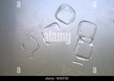 Abstrakte zufällige Formen von ice cube Markierungen auf ein weißes Glas mit Wassertropfen. Abkühlung in heißen Sommertagen - Konzept. Stockfoto