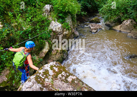 Weibliche Touristen mit Klettersteig Gang über ein Kabel Abschnitt oben Paraul Racilor in Floreşti/Copaceni Schlucht, Rumänien, neben einem kleinen Wasserfall. Kleinen baue Stockfoto