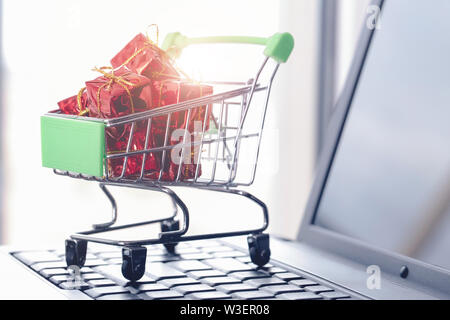 Online shopping Konzept. Warenkorb, kleine Geschenkboxen, Laptop auf dem Schreibtisch Stockfoto