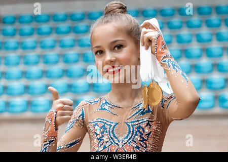 Sieger der rhythmischen Gymnastik Wettbewerb, Porträt einer hübschen kleinen Mädchen, dass in der Hand zwei Goldmedaille und gestikulierend durch Daumen hoch Ein gute Laune Stockfoto