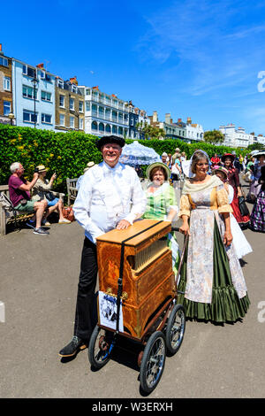 Broadstairs Dickens Festival. Die Menschen gekleidet im viktorianischen Kostümen. Mann, organ Grinder, mit zwei Damen in einer Parade entlang der Promenade. Stockfoto