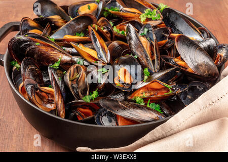 Marinara Muscheln, Moules Mariniere, in einem großen Kochtopf, Nahaufnahme auf einem dunklen Holzmöbeln im Landhausstil Hintergrund Stockfoto