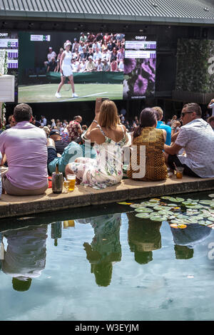 2019 Wimbledon Zuschauer große Bildschirme von Henman Hill/Murray mount, Karpfen Teich im Vordergrund Stockfoto