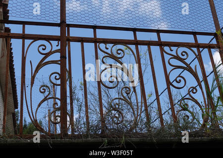 Rostige Geländer mit Blumenmuster und verdorrte Pflanzen auf dem Balkon eines verlassenen Hauses. Stockfoto