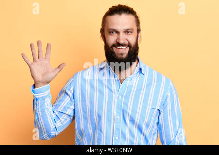 Positiv super schöner Mann im gestreiften Hemd bekleidet und Sagen hallo, seine Hand winken, Körpersprache, isolierte gelben Hintergrund. studio Shot Stockfoto