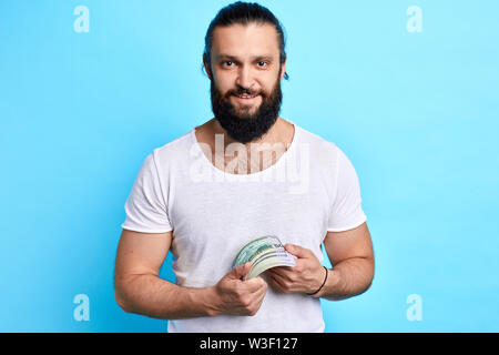 Portrait von fröhlicher junger Mann beiläufig Holding Bündel geld Banknoten über blau Hintergrund isoliert, isolierte blauen Hintergrund, Studio shot Stockfoto