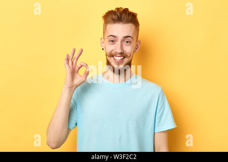 Erfolgreiche aufgeregt Mann mit lustigen Schnurrbart steht auf einem gelben Hintergrund und zeigt ok Zeichen. nach oben Porträt schließen. Ist alles ok. Körper la Stockfoto