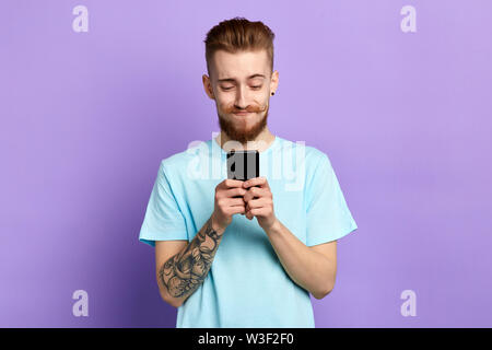 Gerne stilvolle lustig, gut aussehenden Mann mit der Eingabe von SMS auf blauen Hintergrund. nach oben Porträt schließen. Isolierte blauen Hintergrund. Studio gedreht. Stockfoto
