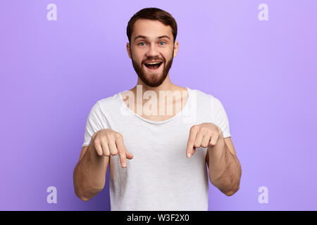 Schöne positive bärtiger Mann nach unten mit zwei Fingern. nach oben Porträt schließen. Isolierte blauen Hintergrund. Studio erschossen. Schauen Sie hier Stockfoto