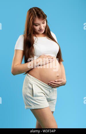 Glücklich super Frau mit langen braunen Haaren ihre Schwangerschaft genießen. Mutterschaft, Elternschaft. Isolierte blauen Hintergrund. studio Shot Stockfoto