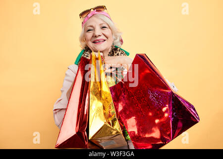 Positive alte Dame genießen neue Kleidung, isolierte gelben Hintergrund, Studio erschossen. Glück Stockfoto