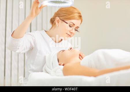 Kosmetikerin Lächeln in der Kosmetologie. Ein Cosmetologist macht ein Gesicht Maske für einen Patienten in einem kosmetologie Klinik. Stockfoto