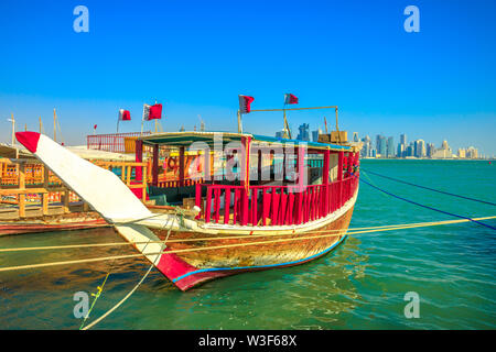 Blick von einem traditionellen hölzernen Dhow mit Qatari Flagge im Vordergrund mit Küste von Doha Bucht und Wolkenkratzer von West Bay Skyline. Hauptstadt Stockfoto