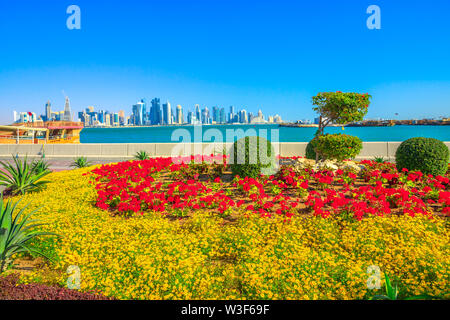 Frühling Landschaft von Blumenbeeten und blühende Bäume auf Corniche Bucht von Doha in Katar. Hohe Wolkenkratzer von Doha Downtown Skyline auf Abstand Stockfoto