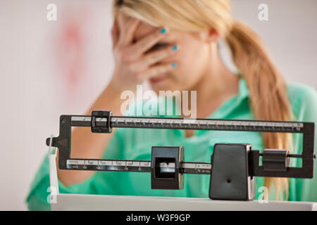 Junge Frau, die ihre Augen mit Verzweiflung während der Verwendung von medizinischen Waagen. Stockfoto