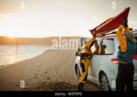 Gerne älteres Paar Anheben einer Sea Kayak auf das Dach eines SUV auf einen Sandstrand geparkt. Stockfoto