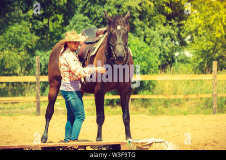 Die Pflege der Tiere, Reiten, equine Konzept. Cowgirl erhalten Pferd bereit für die Fahrt auf die Landschaft. Stockfoto