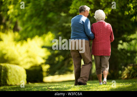 Liebevolle ältere Paare gehen in einen sonnigen Garten zusammen. Stockfoto
