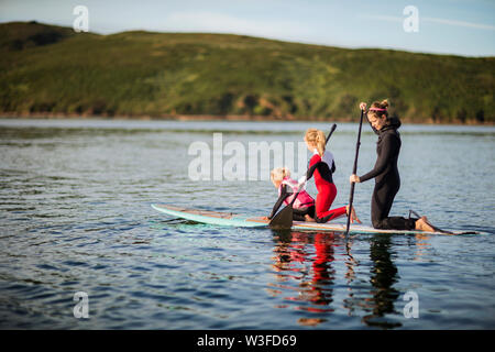 Junge Frau und ihre zwei Töchter zusammen paddleboarding auf einem See. Stockfoto