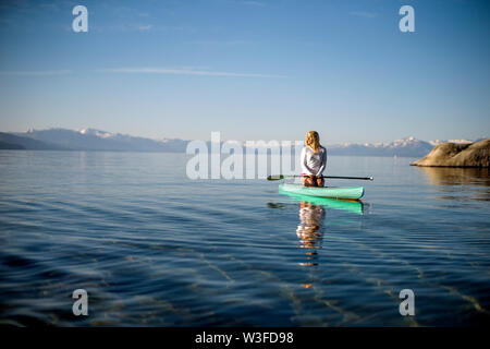 Aktive junge Frau paddleboarding über einen See. Stockfoto